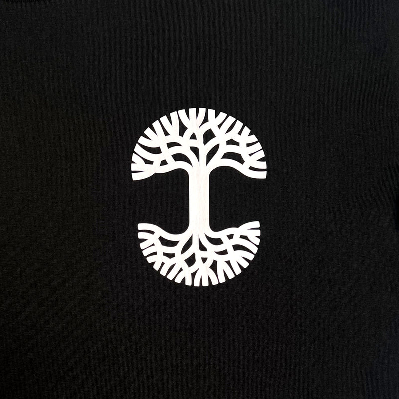 Detailed close up image of black tee with white(to start) UV activated Oaklandish tree logo on wearer's left chest.