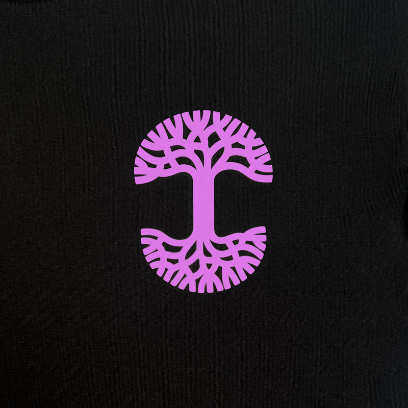 Detailed close up image of black tee with magenta UV activated Oaklandish tree logo on wearer's left chest.