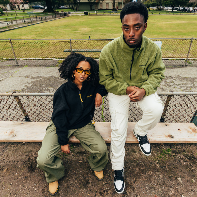 A man and a woman sitting outdoors wearing 1/2 zip polar fleece pullovers in black and green.