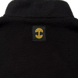 Close-up of a yellow Oaklandish tree logo patch under the collar of a black polar fleece pullover.