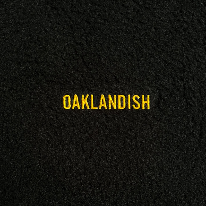 Close-up of yellow embroidered Oaklandish wordmark on a black polar fleece pullover.