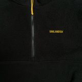 Close-up of yellow embroidered Oaklandish word mark and ½ zip with yellow zip pull on a black polar fleece pullover.