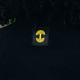 Detail close up of Oaklandish tree logo in yellow on a black satin patch on back of black polar fleece.