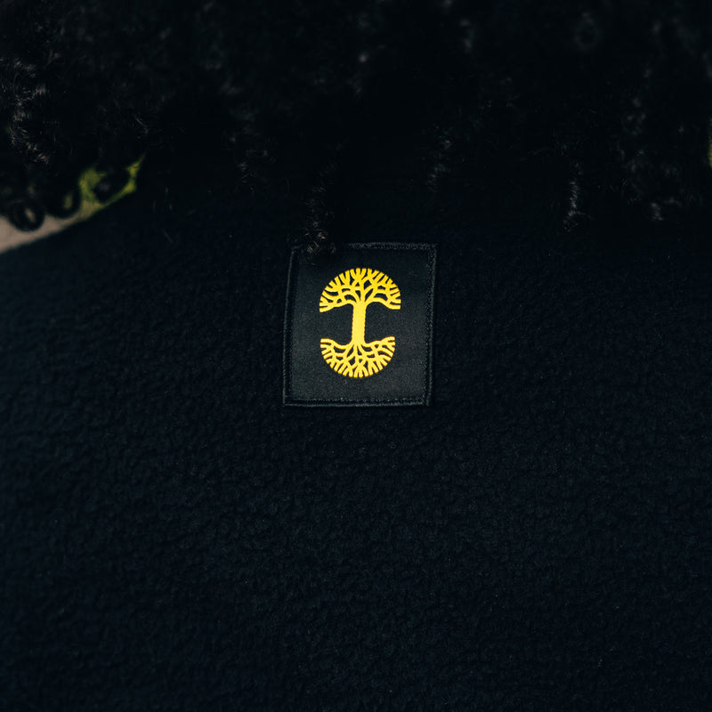 Detail close up of Oaklandish tree logo in yellow on a black satin patch on back of black polar fleece.