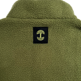Close-up of a black satin logo patch with a green Oaklandish tree logo under the collar of a green polar fleece pullover.