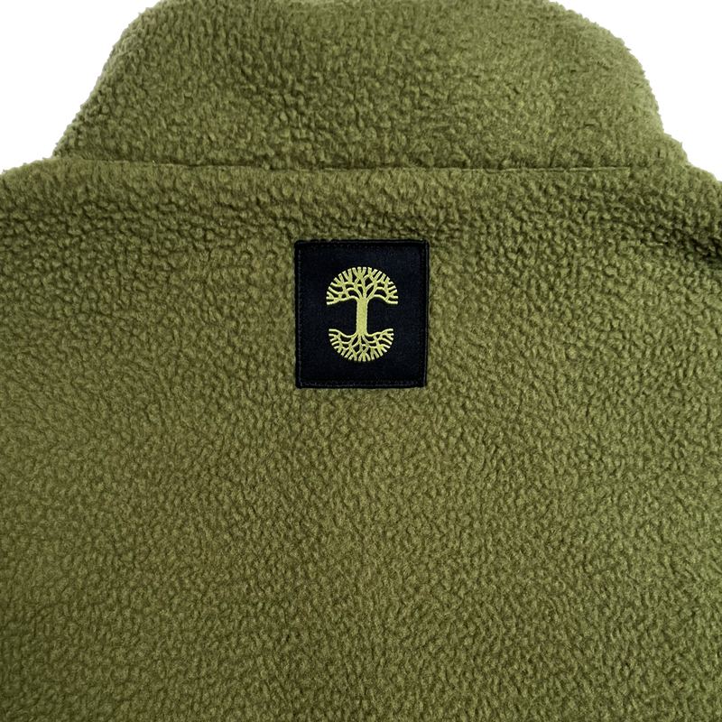 Close-up of a black satin logo patch with a green Oaklandish tree logo under the collar of a green polar fleece pullover.