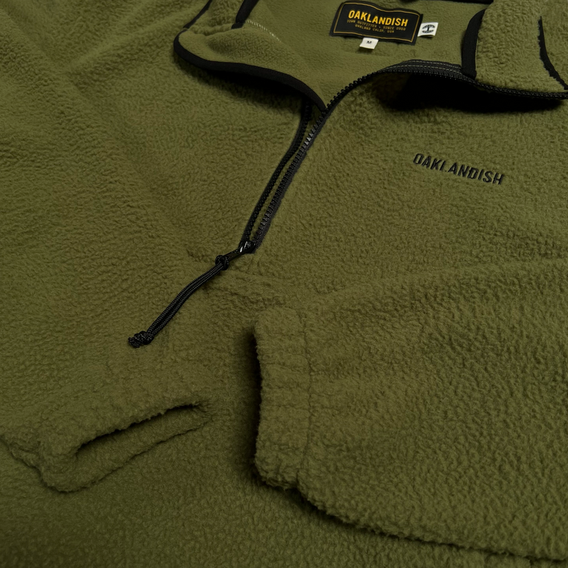 Close up of black 1/2 zip with black pull cord and Oaklandish embroidered wordmark on a green polar fleece.