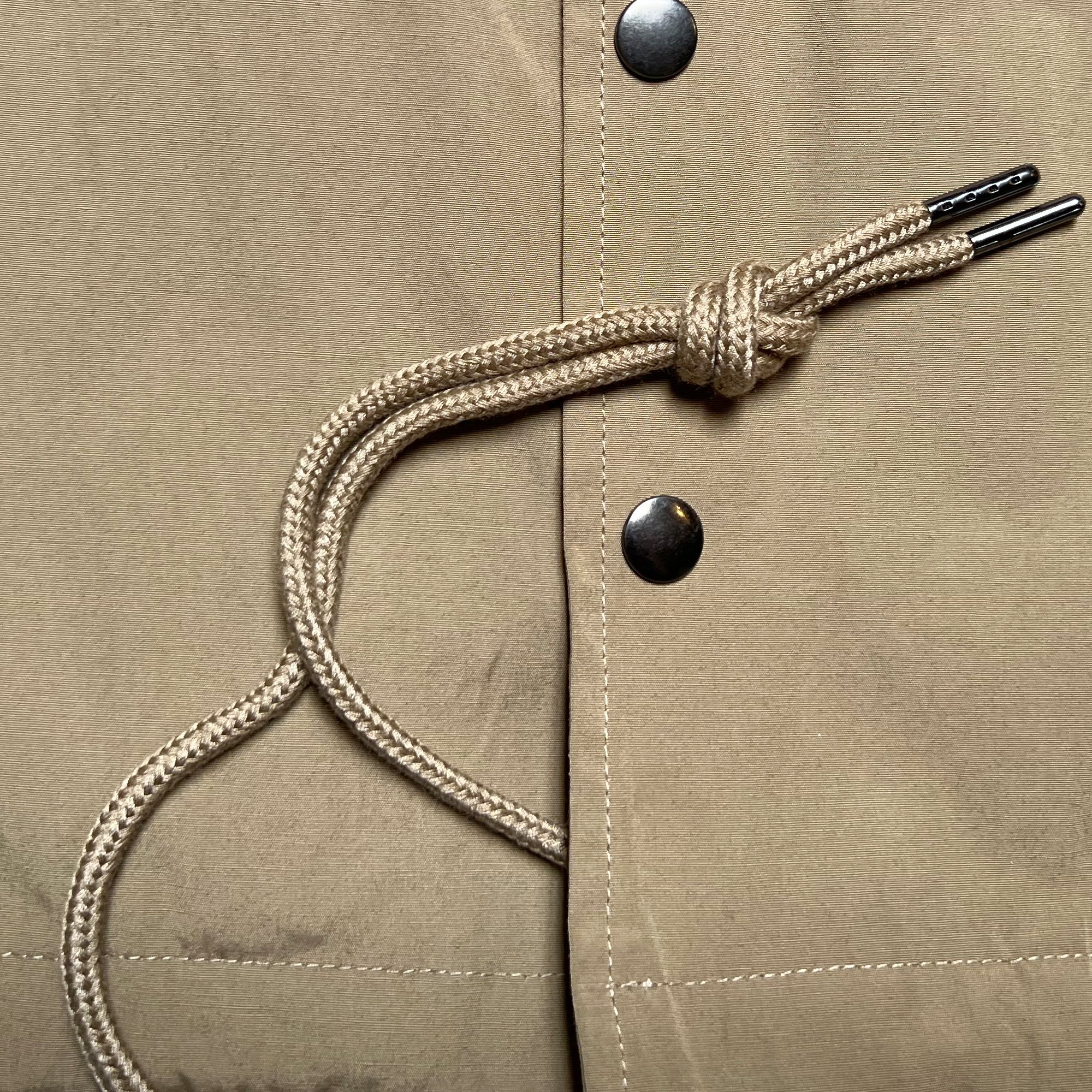 Close up snap closures and waist drawstring on khaki cotton coaches jacket.