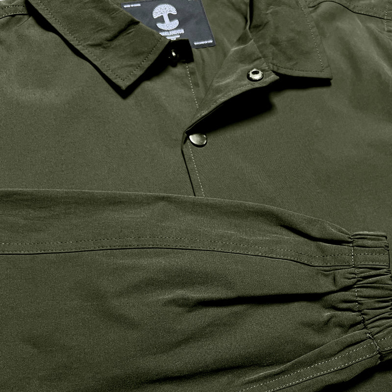 Close up of snap front closure & folded right sleeve of green cotton jacket.