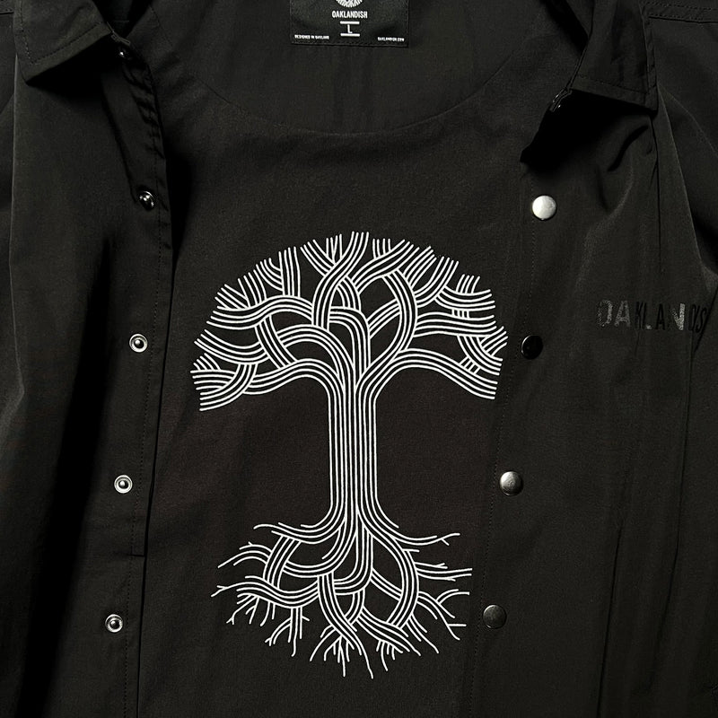 Detailed close-up of large white Oaklandish tree logo on the inside back panel of a black coaches jacket.