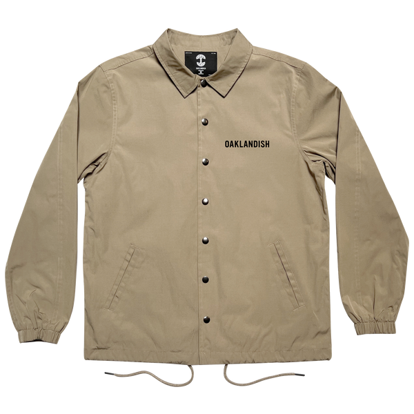 Khaki snap close coaches jacket with 'Oaklandish' wordmark on the wearer's left chest, with a collar and drawstring waist.