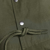 Detailed close up of olive snap closures and waist drawstrings with metal tabs on an olive Oaklandish coaches jacket.