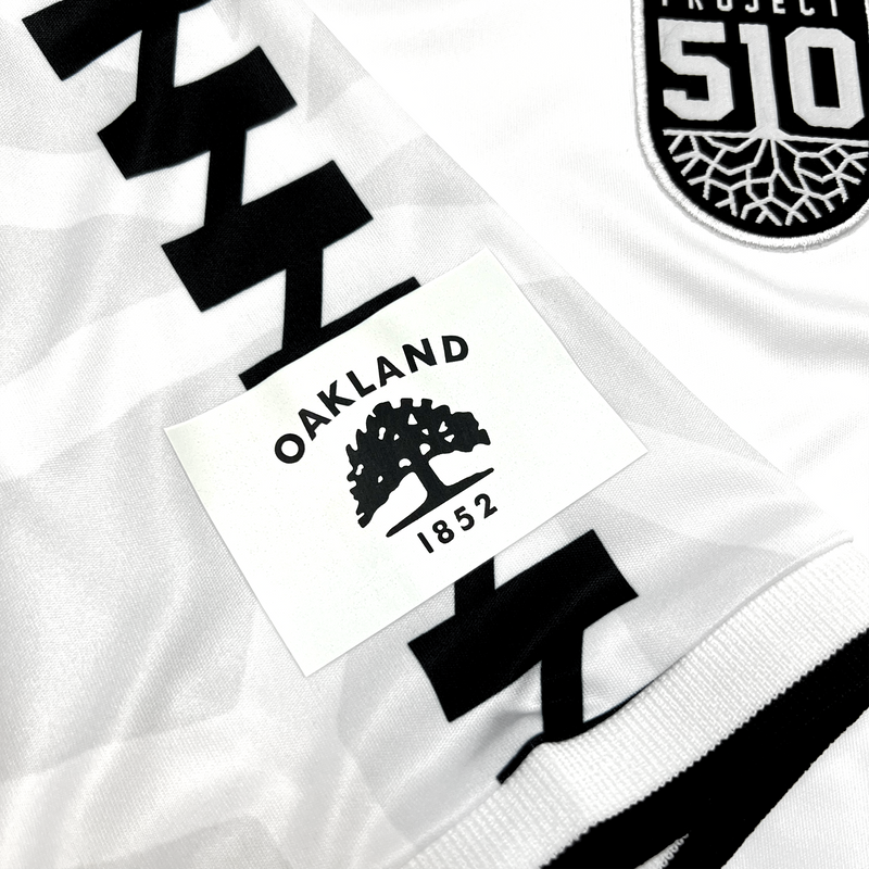 Detail close up of white Meyba jersey Project 510 crest on wearer's left chest and Oakland Flag in Black and white on right sleeve.