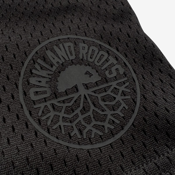 Close up of round Oakland Roots logo on bottom left side of black men’s mesh athletic shorts.