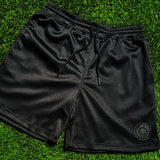 Black men’s mesh athletic shorts with round Oakland Roots logo on bottom left side on green grass.