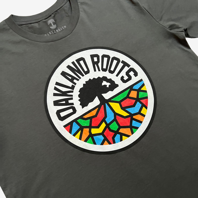 Three-quarter view of a charcoal grey t-shirt with full-color, round Oakland Roots logo on the chest.