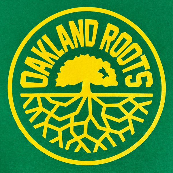 Close-up of large yellow Oakland Roots SC logo crest on a Kelly Green t-shirt.