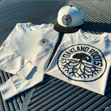 Ecru short sleeve tee, Ecru long sleeve tee and chrome New Era cap with black roots crest on outdoor surface.
