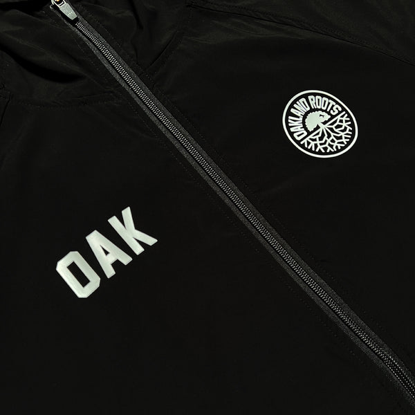Close-up of white OAK wordmark on right chest, and Roots SC round logo on left chest of black zip-up hoodie.