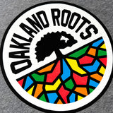 Close up of full-color, round Oakland Roots logo on the chest of an athletic grey t-shirt. 