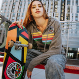 Woman outside holding skateboard wearing gunmetal heather full zip hoodie with colored stripes and full-circle Roots SC mosaic logo.