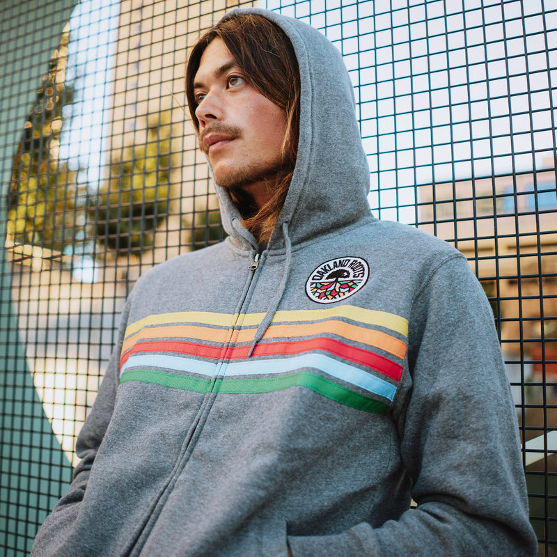 Man outside wearing gunmetal heather full zip hoodie with colored stripes and full-circle Roots SC mosaic logo.
