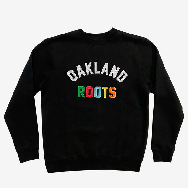 Black crew neck sweatshirt with white “OAKLAND” applique wordmark and full-color “ROOTS” wordmark underneath on chest.