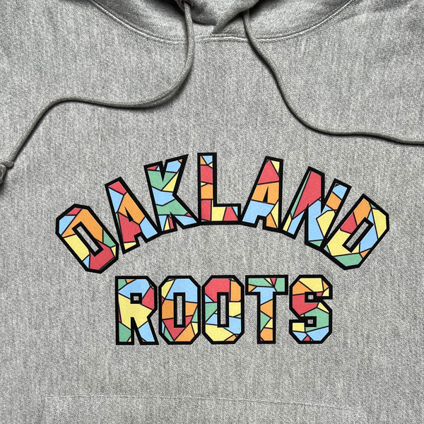 Close up of Oakland Roots applique wordmark in rainbow capital letters on grey hoodie.