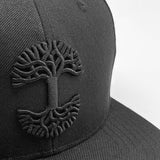 Close-up of black embroidered Oaklandish tree logo on a black cap.