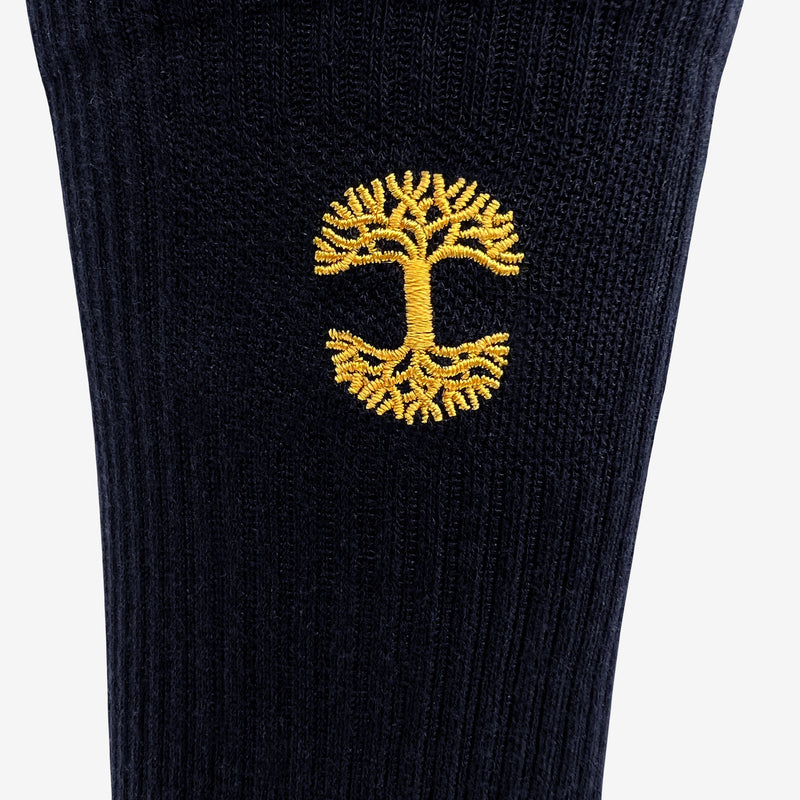 Close up of gold embroidered Oaklandish logo at the top of black crew socks.