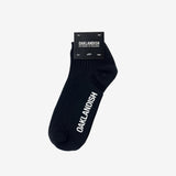 Low-cut slate black crew socks with a white Oaklandish wordmark on the sole folded in packaging.