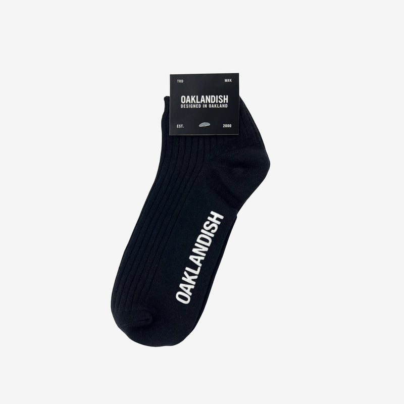 Low-cut slate black crew socks with a white Oaklandish wordmark on the sole folded in packaging.