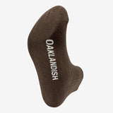  Low-cut slate brown crew socks showing a close-up view of a white Oaklandish wordmark on the sole.