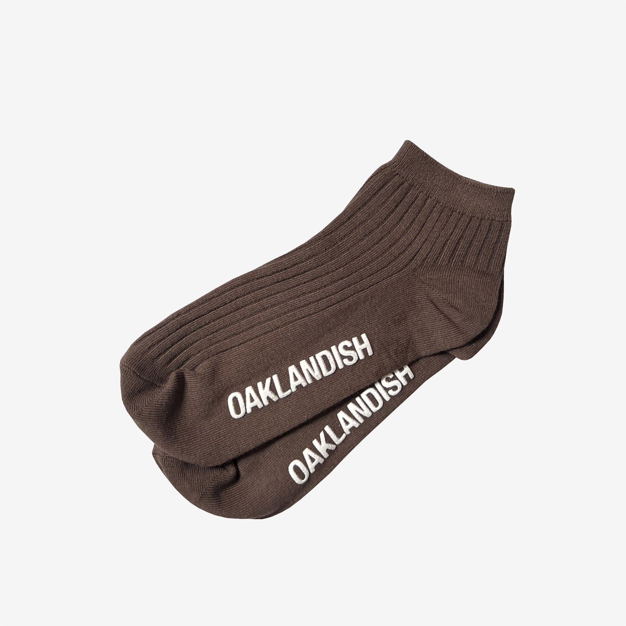 Side view of low-cut slate brown crew socks with a white Oaklandish wordmark on the sole.