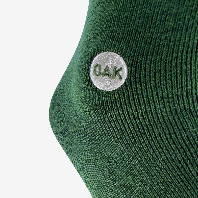 Close up of the embroidered Oak wordmark detail on a plush green men’s crew sock.