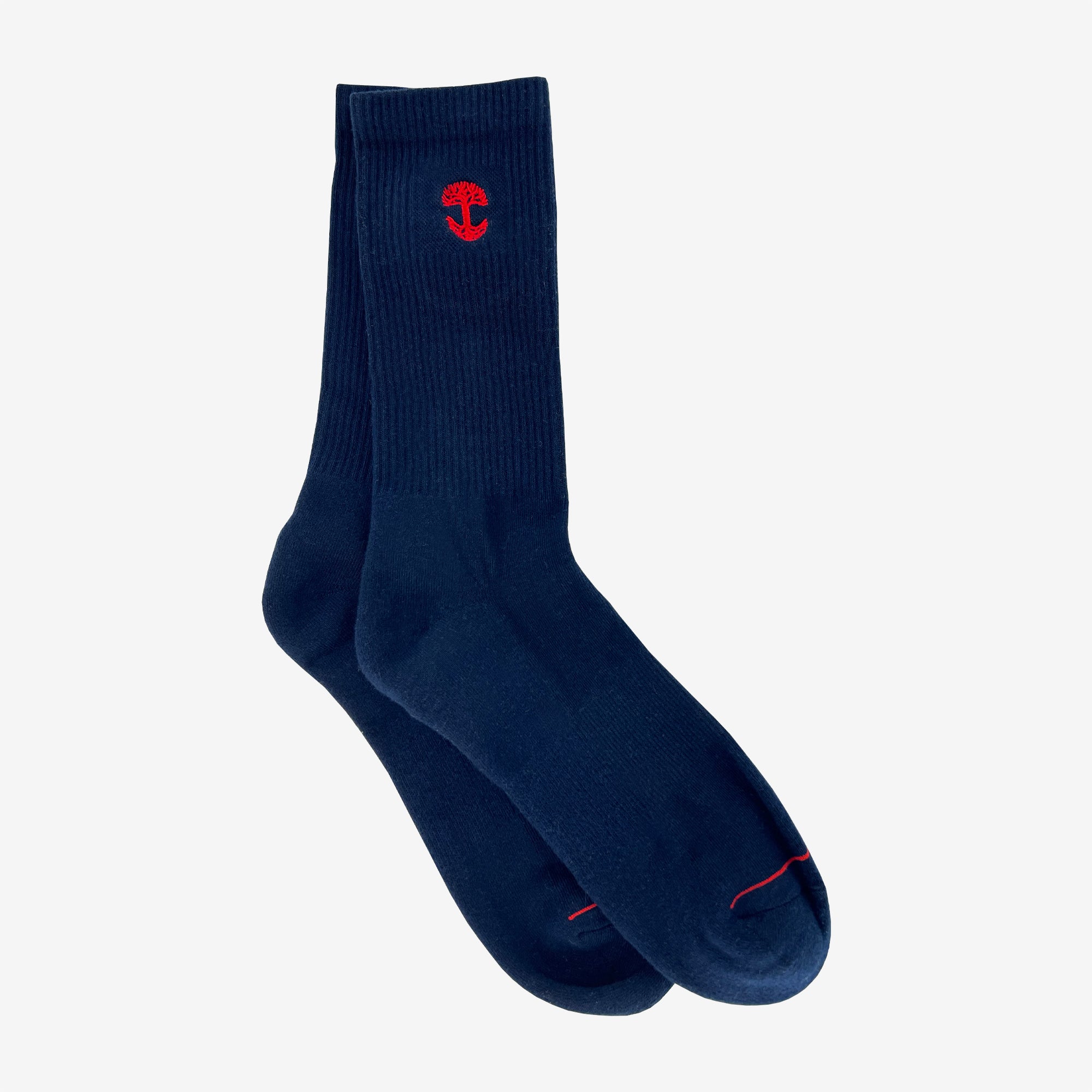A pair of Embroidered Logo Socks from Oaklandish, in a deep navy blue color with a ribbed texture near the top. Each sock showcases a small red tree emblem, similar to the Oaklandish logo, near the cuff. The adult-size socks are slightly overlapped, with one sock's toe resting on the other's cuff, all set against a plain light grey background.