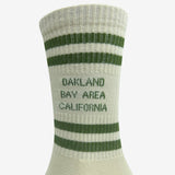 Close up of Oakland Bay Area California printed in green capital letters on white crew socks.