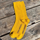 High cut yellow men's crew socks with Oaklandish wordmark in brown on sole. Socks positioned on wooden bench.