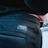 Detail close-up of the Oaklandish logo patch above the zippered back pocket on man wearing black joggers.