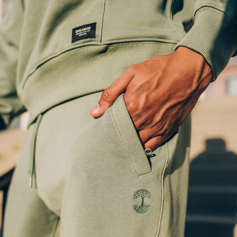 Detailed close of a man’s hand in the front pocket of black Oaklandish joggers with Oaklandish tree logo.
