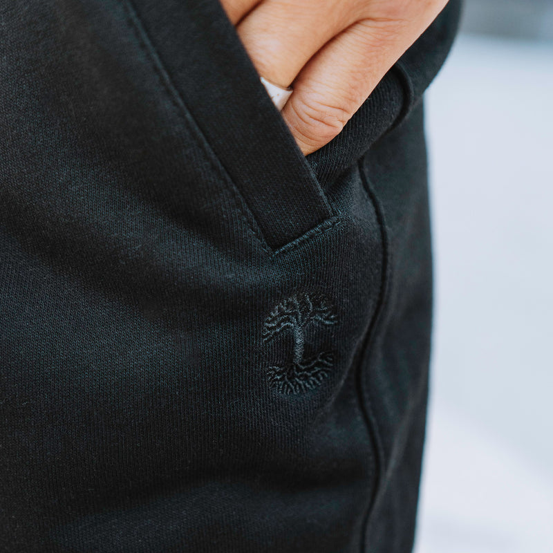 Detailed close of a person’s hand in the front pocket of black Oaklandish joggers.