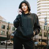 Woman outside wearing a black Oaklandish hoodie and jogger set.