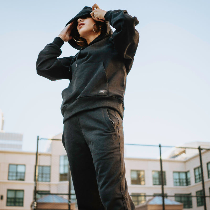 Woman outside wearing a black Oaklandish hoodie and jogger set.