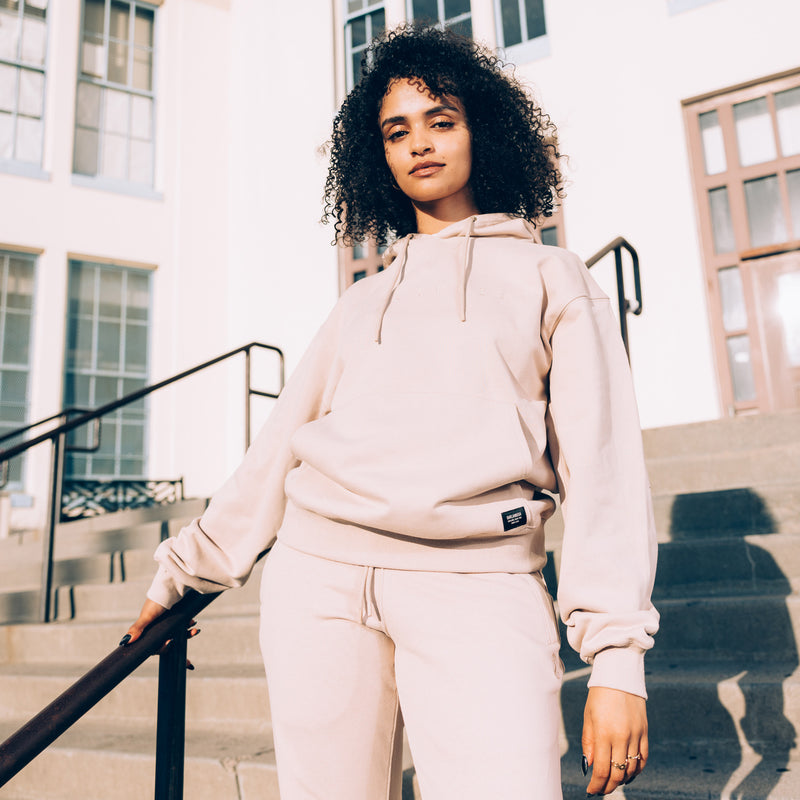Woman standing outside in a sand-colored Oaklandish hoodie and jogger set. 
