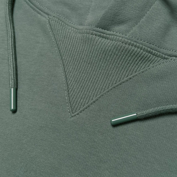 Detailed close up of triangle ribbing patch at collar of army green pullover hoodie with metal drawcord tips.