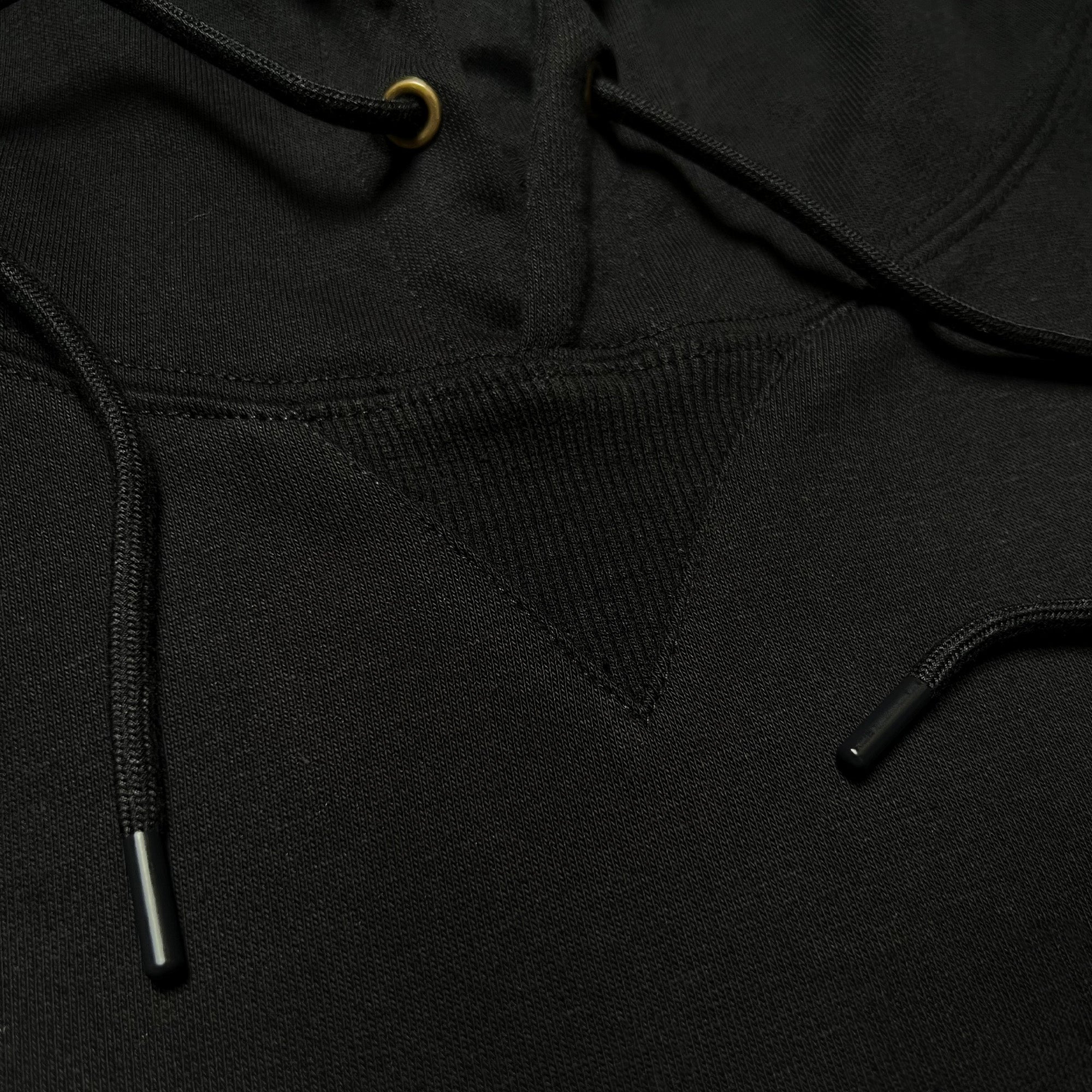 Detailed close up of triangle ribbing patch at collar of black pullover hoodie with metal drawcord tips.