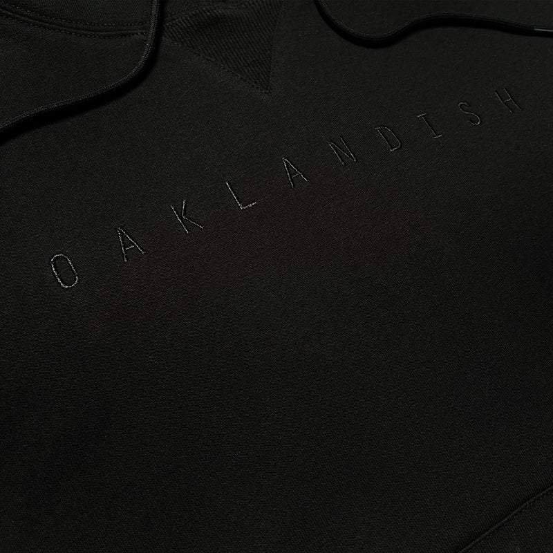 Detailed close-up of black pullover sweatshirt with monochromatic Oaklandish wordmark embroidered on chest.