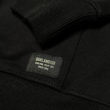 Detailed close up of Oaklandish label on left corner of black hoodie and cuff ribbing on end of sleeve. 