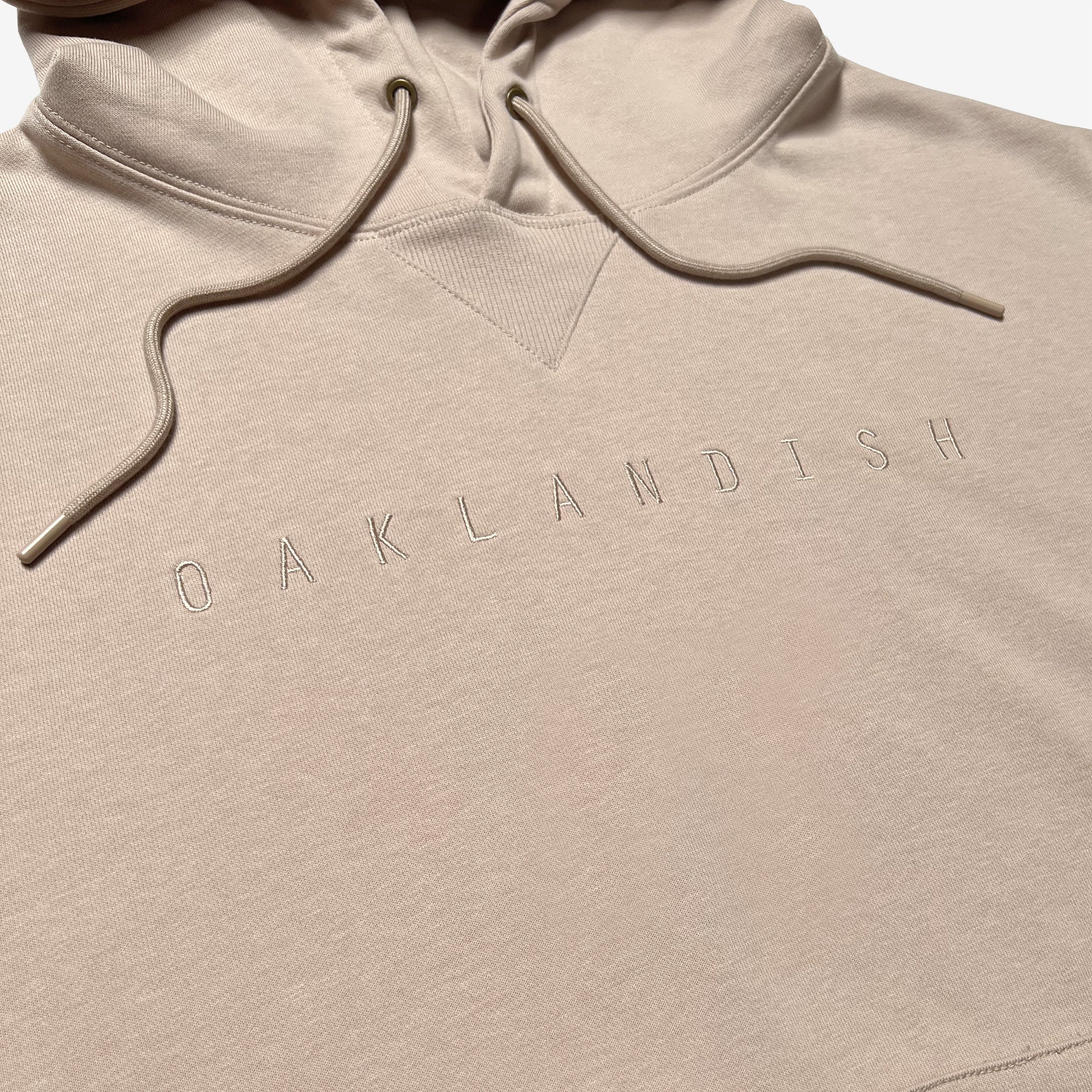 Detailed close-up of embroidered Oaklandish wordmark on a sand-colored hoodie.
