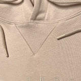 Detailed close up of triangle ribbing patch at collar of a sand hooded sweatshirt with metal drawcord tips.